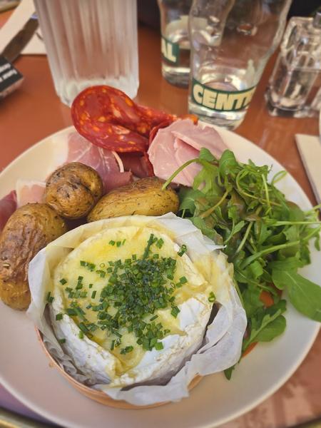 Un camembert chaud avec pommes de terre, salade et charcuterie.