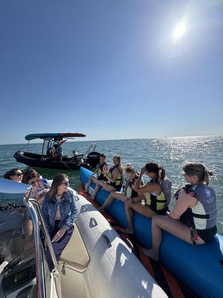 Un groupe de femmes sur une bouée tractée banane, un autre groupe sur un bateau à moteur.