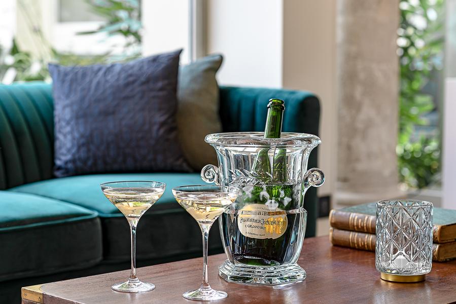 Une bouteille de champagne et deux verres servies sur une table basse, devant un canapé bleu.