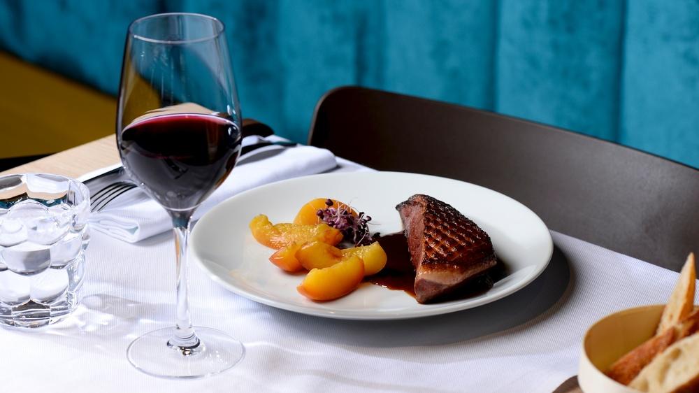 Une assiette avec un magret de canard et accompagnement, et un verre de vin rouge