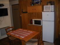 Coin séjour et cuisine avec table à manger, four à micro-ondes, TV, ameublement bois et parquet au sol