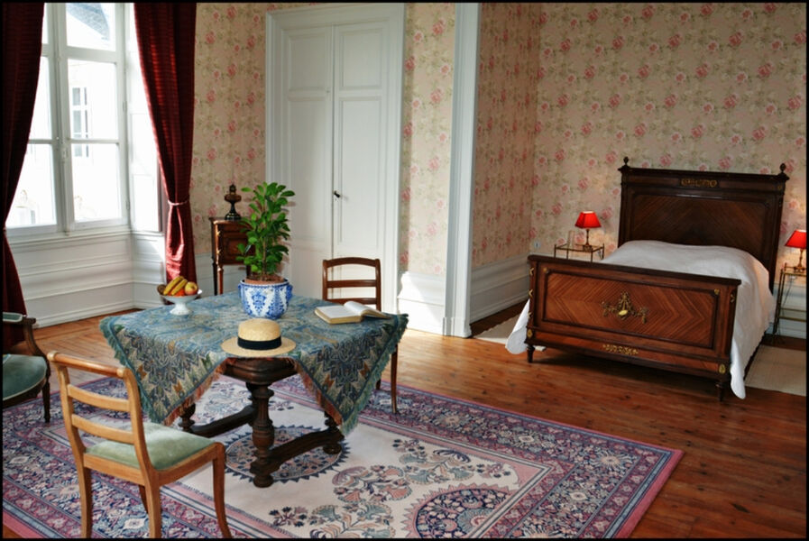 Chambre tapissée dans les tons orangés avec parquet, lit double et petit salon