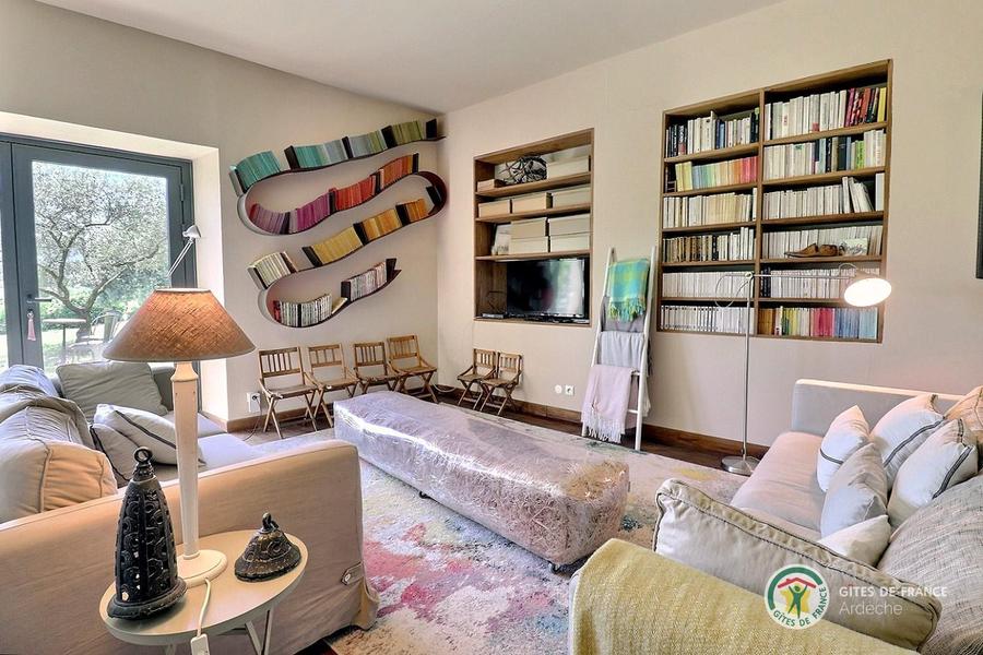 Le salon avec canapés, fauteuils, bibliothèque, cheminée et TV