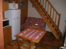 Coin séjour et cuisine avec table à manger, canapé, four à micro-ondes, TV, ameublement bois et parquet au sol, escalier vers l'étage supérieur