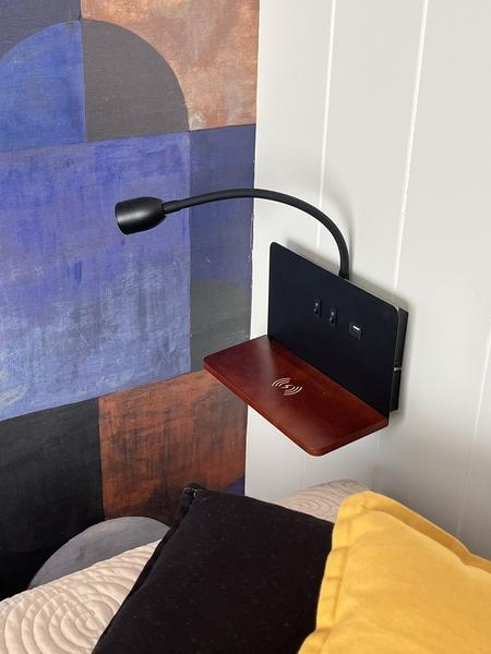 Un table de chevet indiquant une recharge d'apparail sans fil, et une lampe,