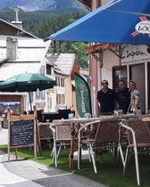 Terrasse extérieure du restaurant dans la grand-rue d'Allos, fausse pelouse, tables et chaises, parasols