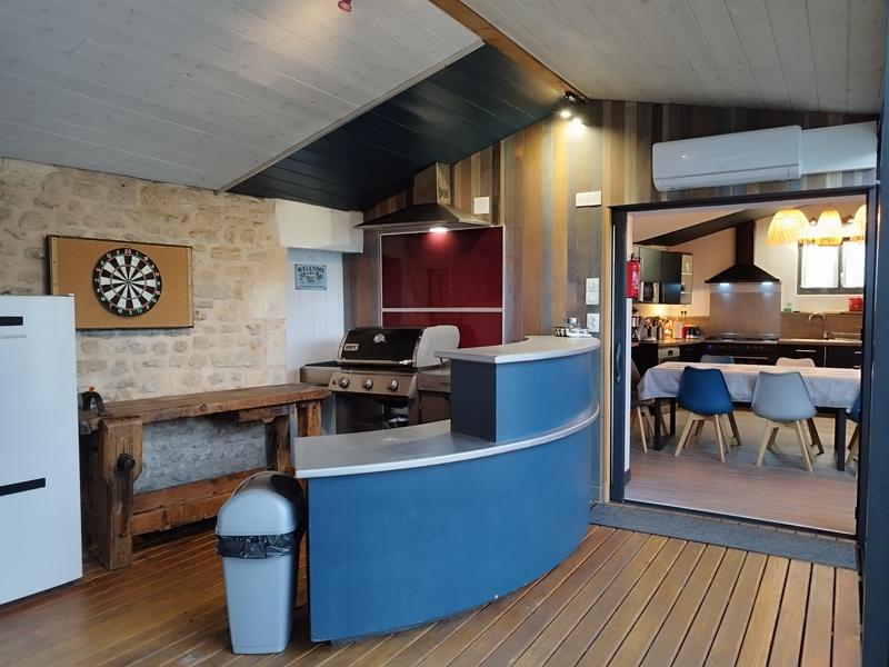 Un espace bar sous une véranda, avec bar, barbecue, fléchettes, frigo.
