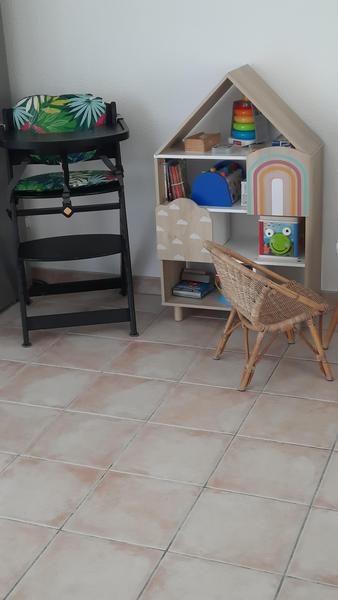 Coin enfant avec chaise haute, petit siège en osier, meuble avec quelques jouets.