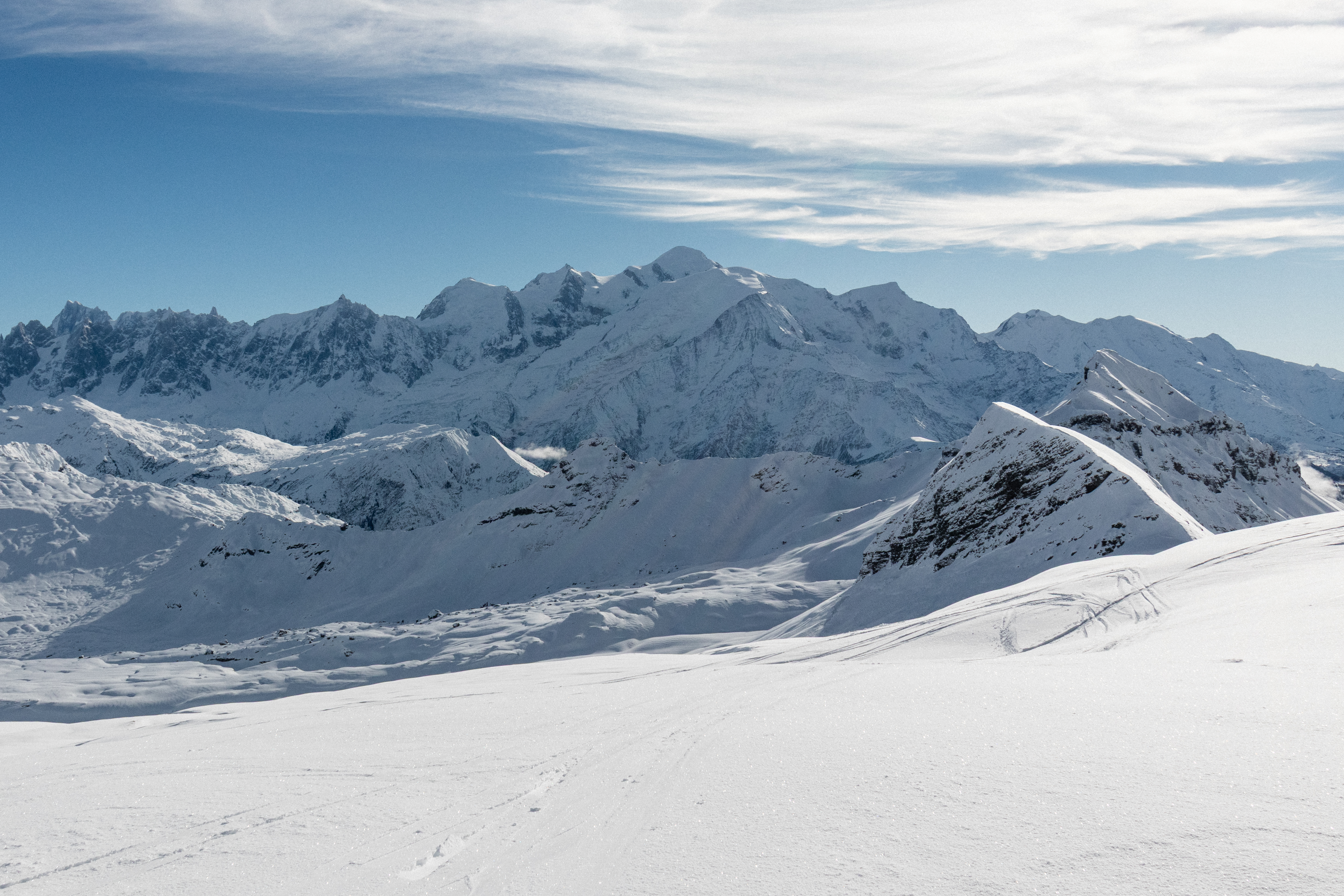 De met sneeuw bedekte top van de Mont Blanc domineert de horizon in het midden van een uitgestrekt Alpenpanorama onder een heldere blauwe lucht.