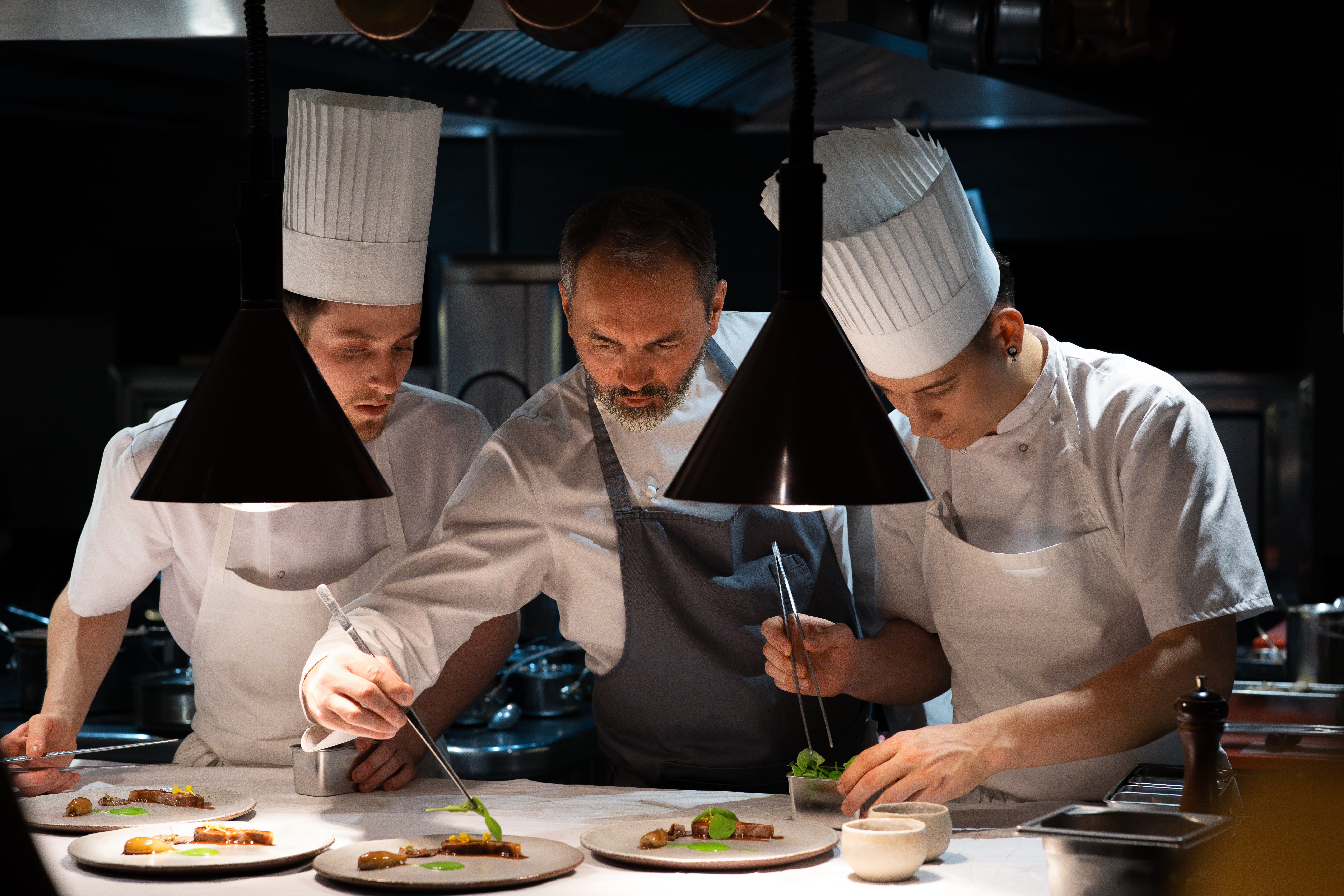 Christophe Aribert préparant un plat entouré de deux cuisiniers