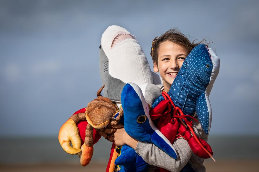 Un enfant tenant dans ses bras des peluches requin, crabe, écrevisse, etc.