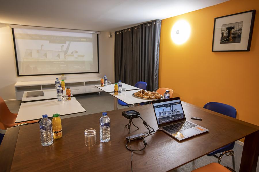 Une salle de réunion avec 5 tables et chaises, un vidéo-projecteur, des bouteilles d'eau et de jus de fruits.