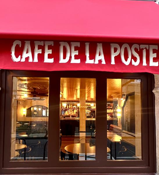 La salle du restaurant vue depuis l'extérieur, avec le store où est inscrit "le Café de la Poste".