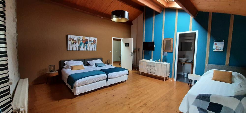 Une grande chambre avec 3 lits simples, au fond une salle d'eau.