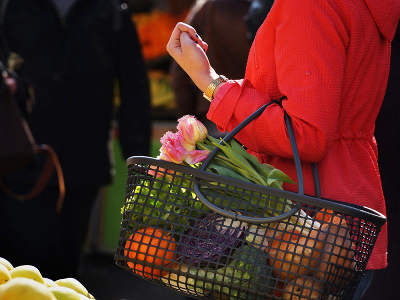 Une dame en rouge tenant un panier en matière de poches ostéricole, dedans des légumes en tout genre et tulipes.