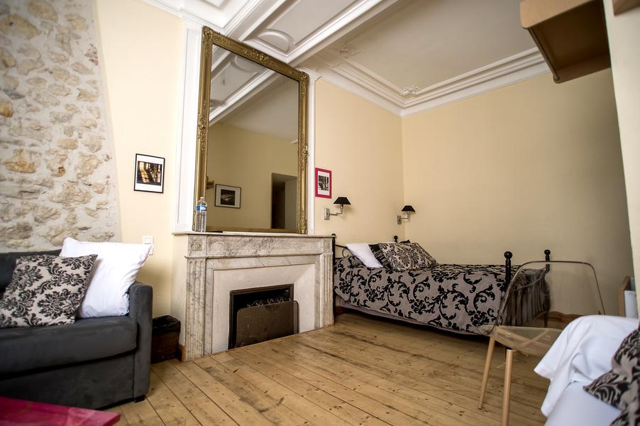 Une chambre avec un lit, une cheminée avec un grand miroir au dessus, un canapé.