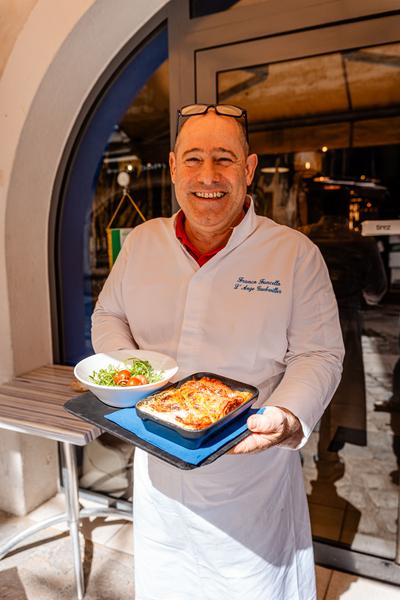 Le chef devant le restaurant, présentant un plat chaud et une salade.