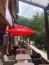Terrasse extérieure du restaurant, dans une cour en dallage, tables et chaises sous parasols rouges