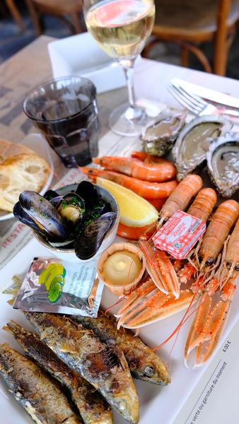 Une assiette avec sardines grillées, huitres, moules, crevettes, langoustines, et un verre de vin.