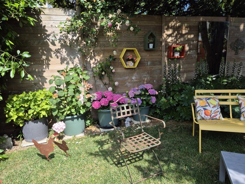 Un coin du jardin avec une chaise et un banc métalliques.