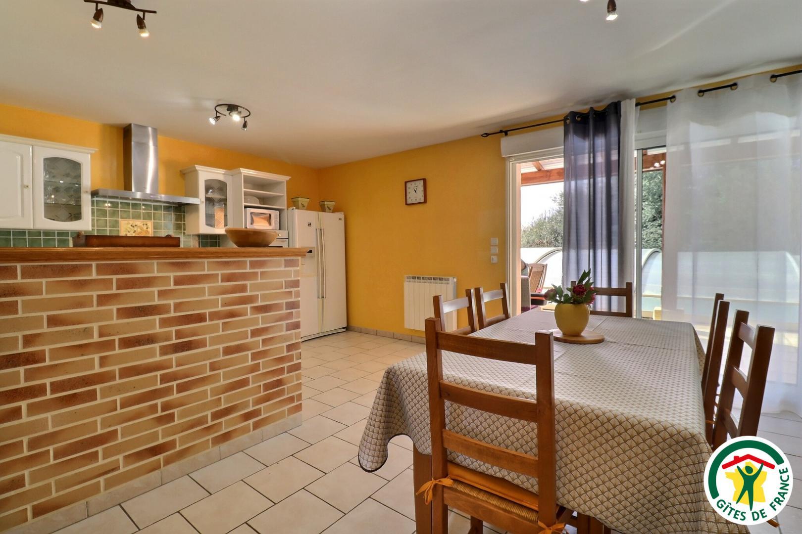 Pièce à vivre : cuisine équipée, espace repas et coin salon TV avec insert.
Accès direct à la terrasse et piscine depuis cette pièce