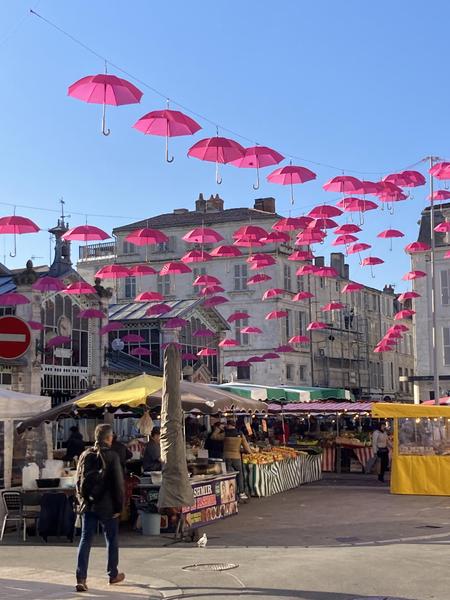La place du marché avec les parapluie roses suspendus pendant "Octobre Rose", à proximité de la boutique.