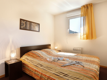 Chambre à coucher d'appartement avec lit double, fenêtre hublot, porte-fenêtre donnant sur balcon