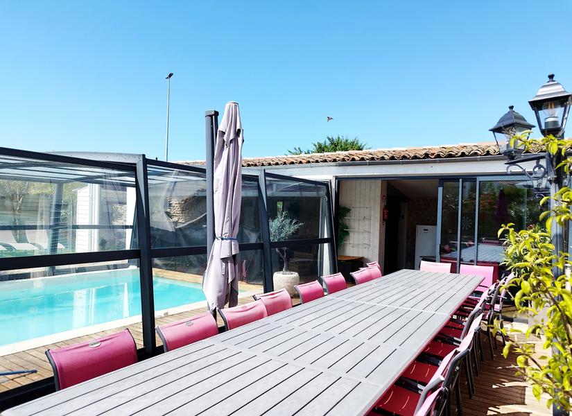 Une grande table en extérieur avec une quinzaine de chaises, la piscine couverte.