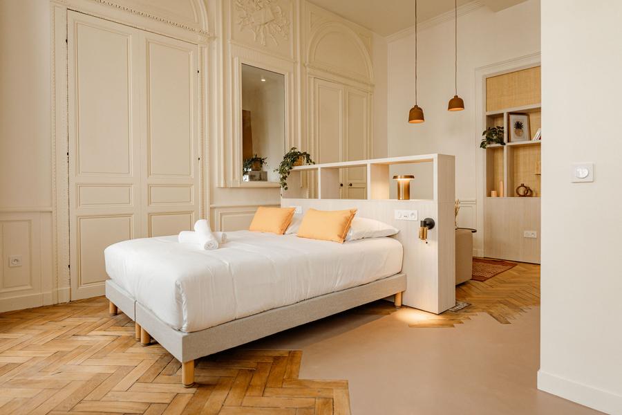 Une chambre avec un lit double, dans une pièce à haut plafond et moulures.
