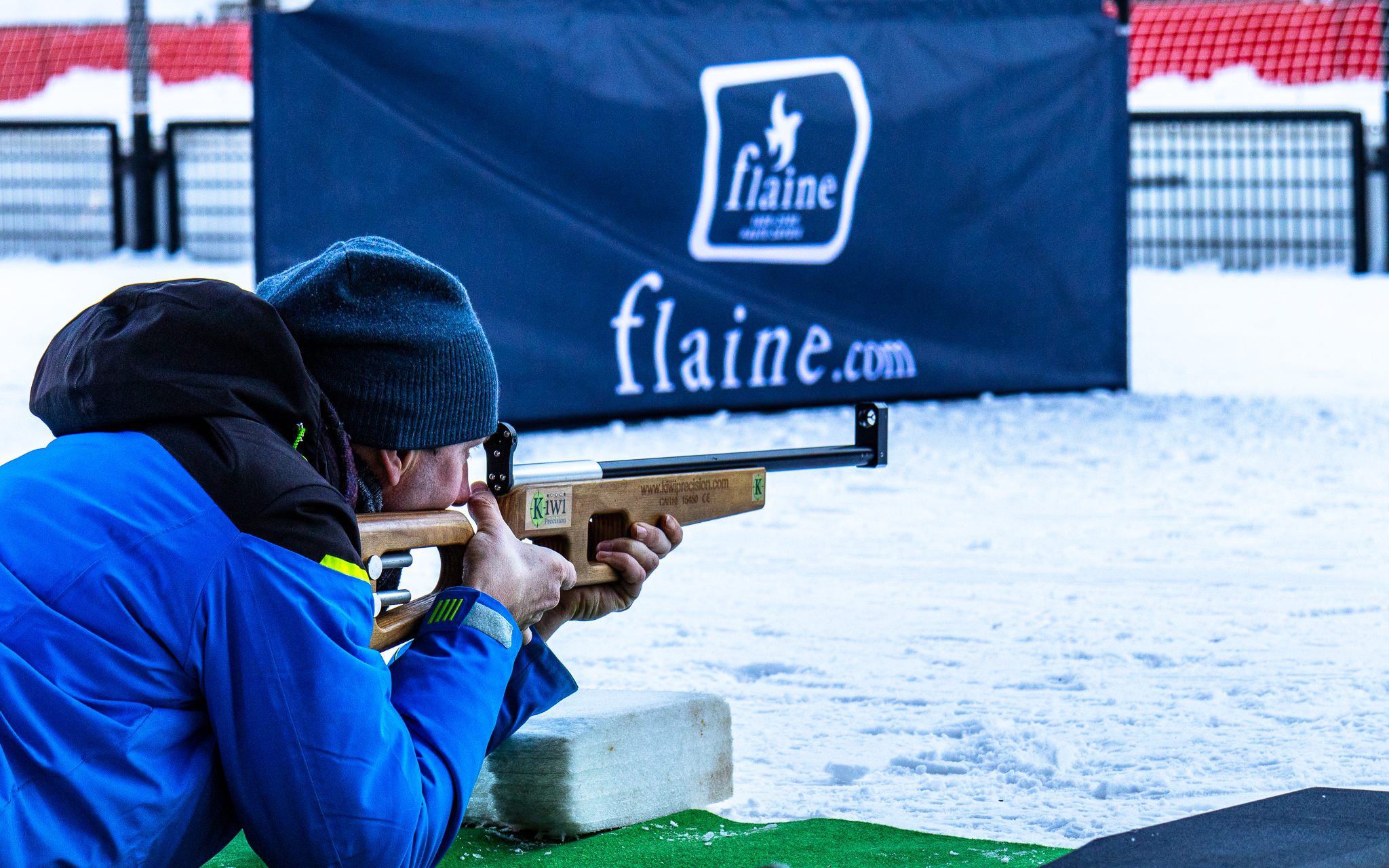 Un tireur s'exerce au tir de précision en position allongée sur la neige, visant avec une carabine devant une bannière de la station de Flaine
