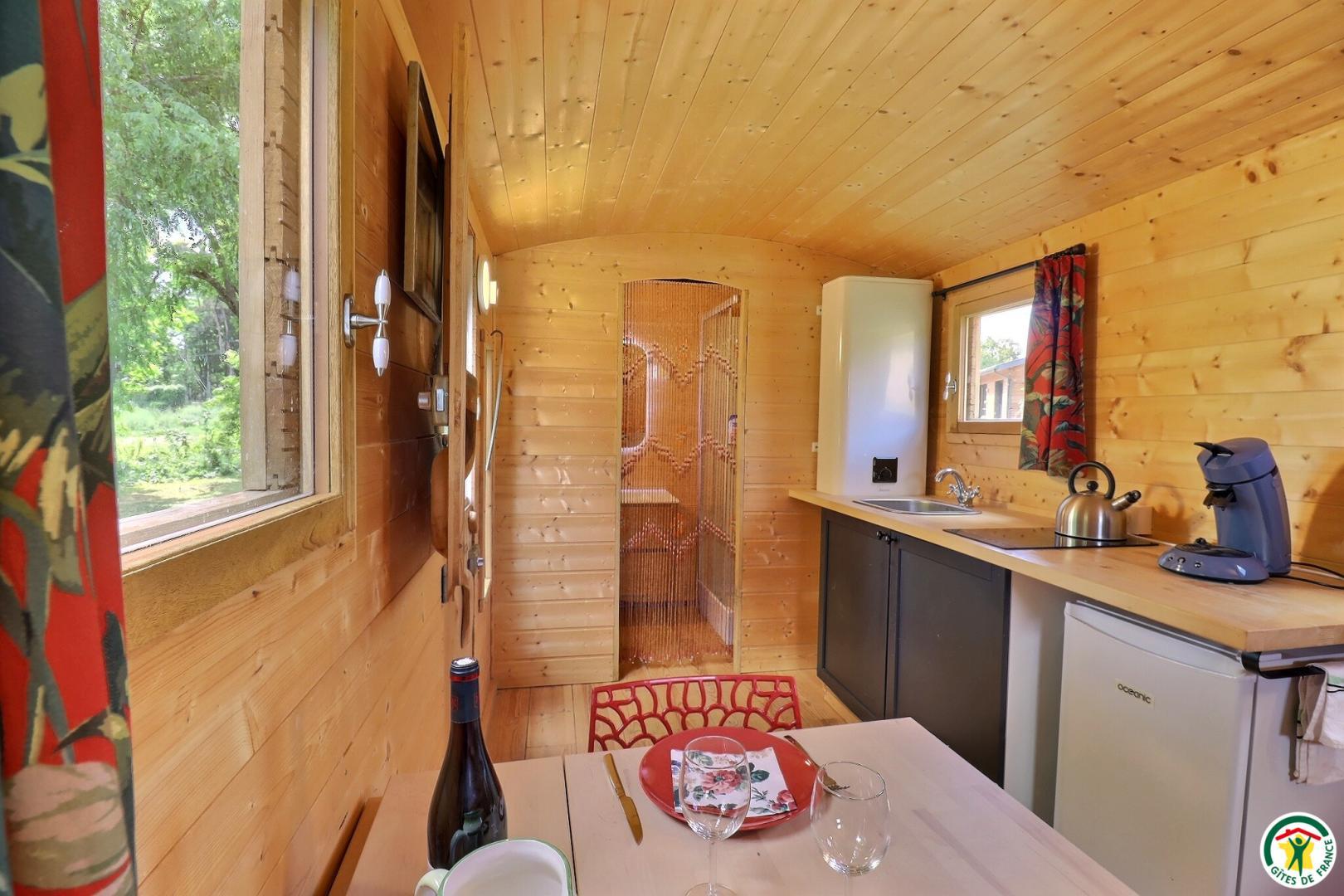 L'intérieur de la roulotte, coin cuisine et espace repas, salle d'eau/wc en arrière plan