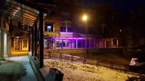 Devanture du restaurant de nuit avec terrasse extérieure avec tables et chaises. Panneau avec inscription : "Pourquoi pas ? Crêperie Pizza" "Spécialités montagnardes"