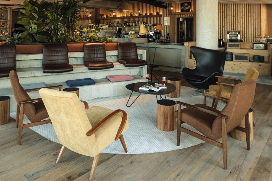 Un espace avec un midi gradin de deux rangs composés de fauteuils et de coussins de sols, des fauteuils et une table basse.