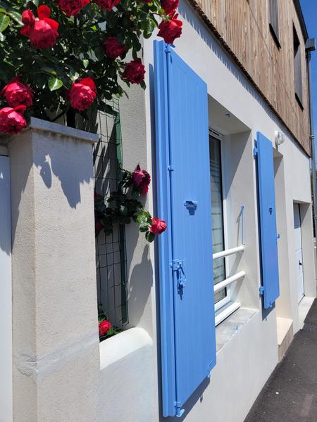 La facade extérrieur de la maison, volets bleu, des roses dépassant d'un grillage.
