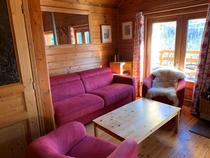 Séjour de chalet en bois avec canapé, fauteuils, table basse, ameublement bois, fenêtre