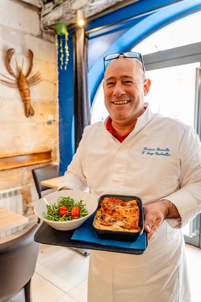 Le chef dans son restaura,t présentant un plat chaud et une salade.