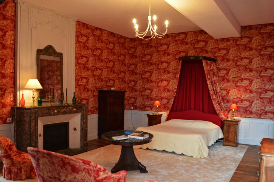 Chambre très spacieuse dans les tons rouge, grand lit surmonté dun rideau, cheminée et petit salon