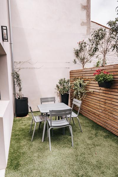 Une petite terrasse avec brise vue en pallissade, fausse herbe, table et 4 chaises métalliques.