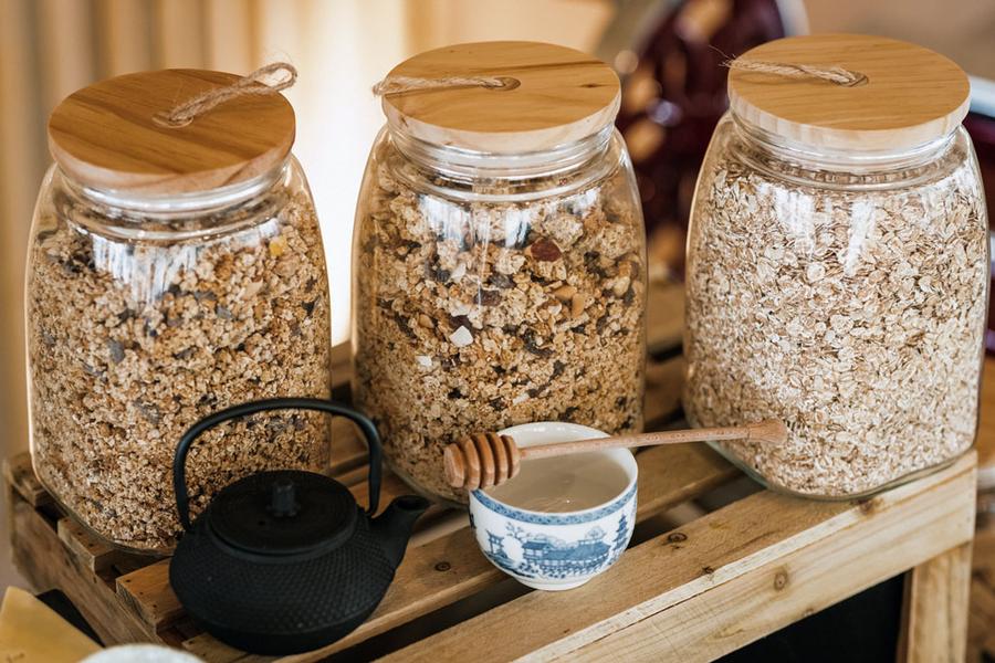 Trois grands pots de différents céréales, une cuillère à miel et une théière.