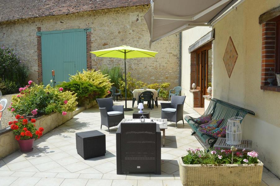 Terrasse coté sud, on aperçoit la table pour prendre les petits déjeuners dehors, à coté du parasol vert et devant la baie vitrée de la pièce des hôtes