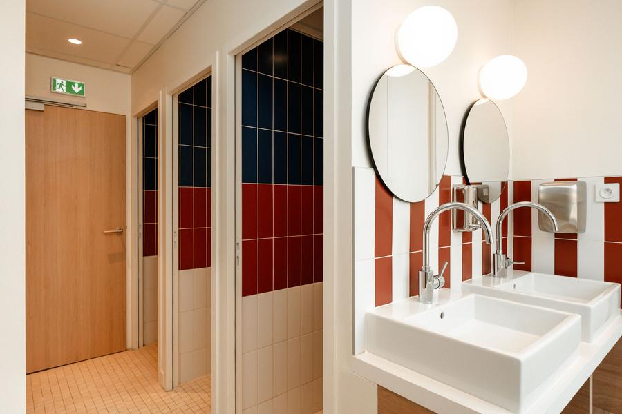 une salle d'eau collective avec 3 douches individuelles fermées, et deux lavabos.