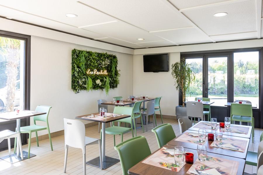 La salle de restaurant de l'hôtel, avec des tables dressées et des chaises en plastiques blanches et vertes.
