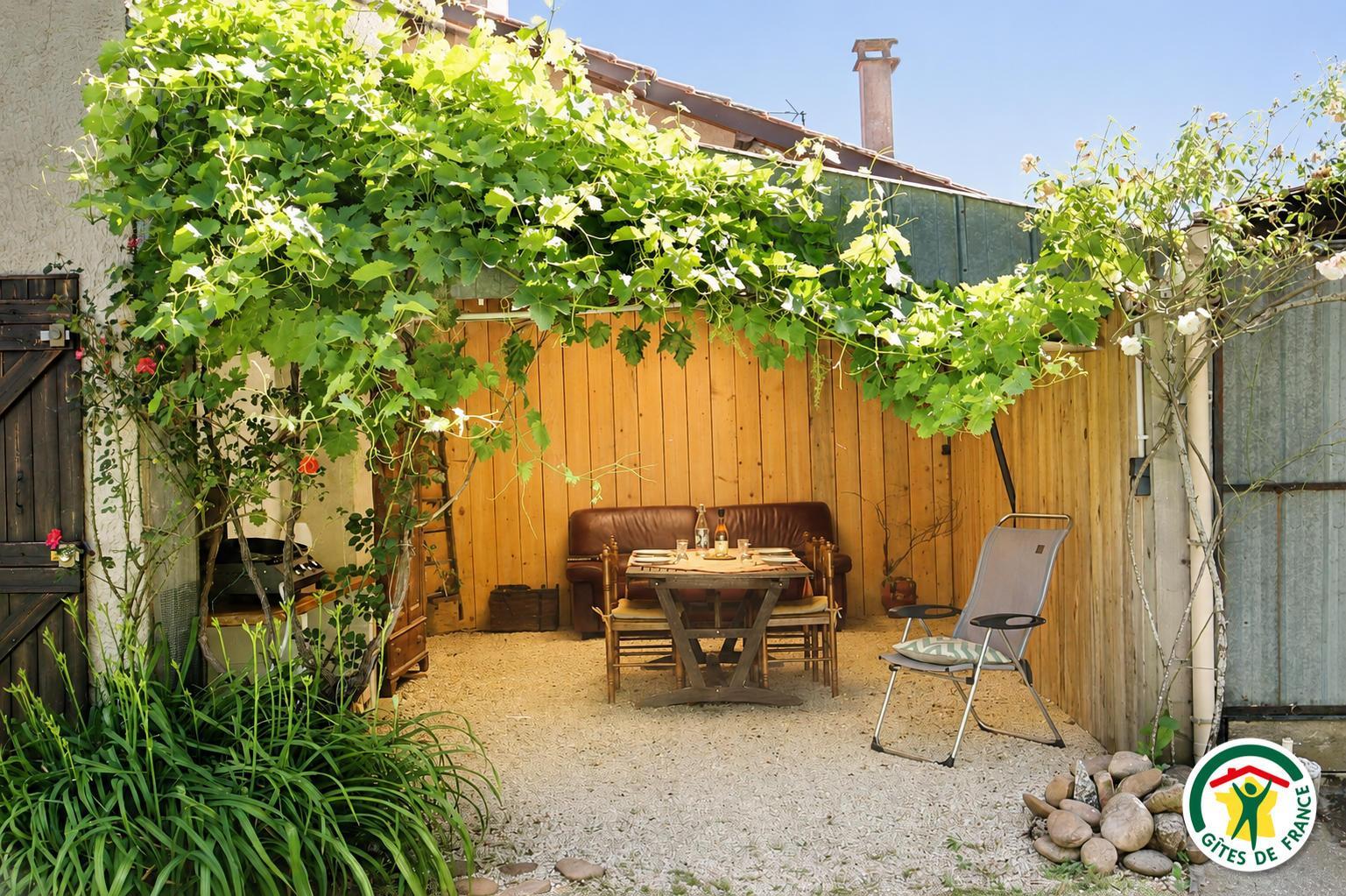 Terrasse couverte d'extérieur avec table, canapé et plancha à disposition.