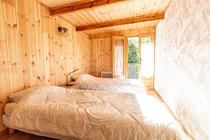 Chambre à coucher lumineuse avec deux lits simples, ameublement bois, parquet au sol, porte-fenêtre