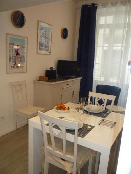 Coin repas avec une table dressée et deux chaises. Au fond de la pièce une commode avec une télé posée.