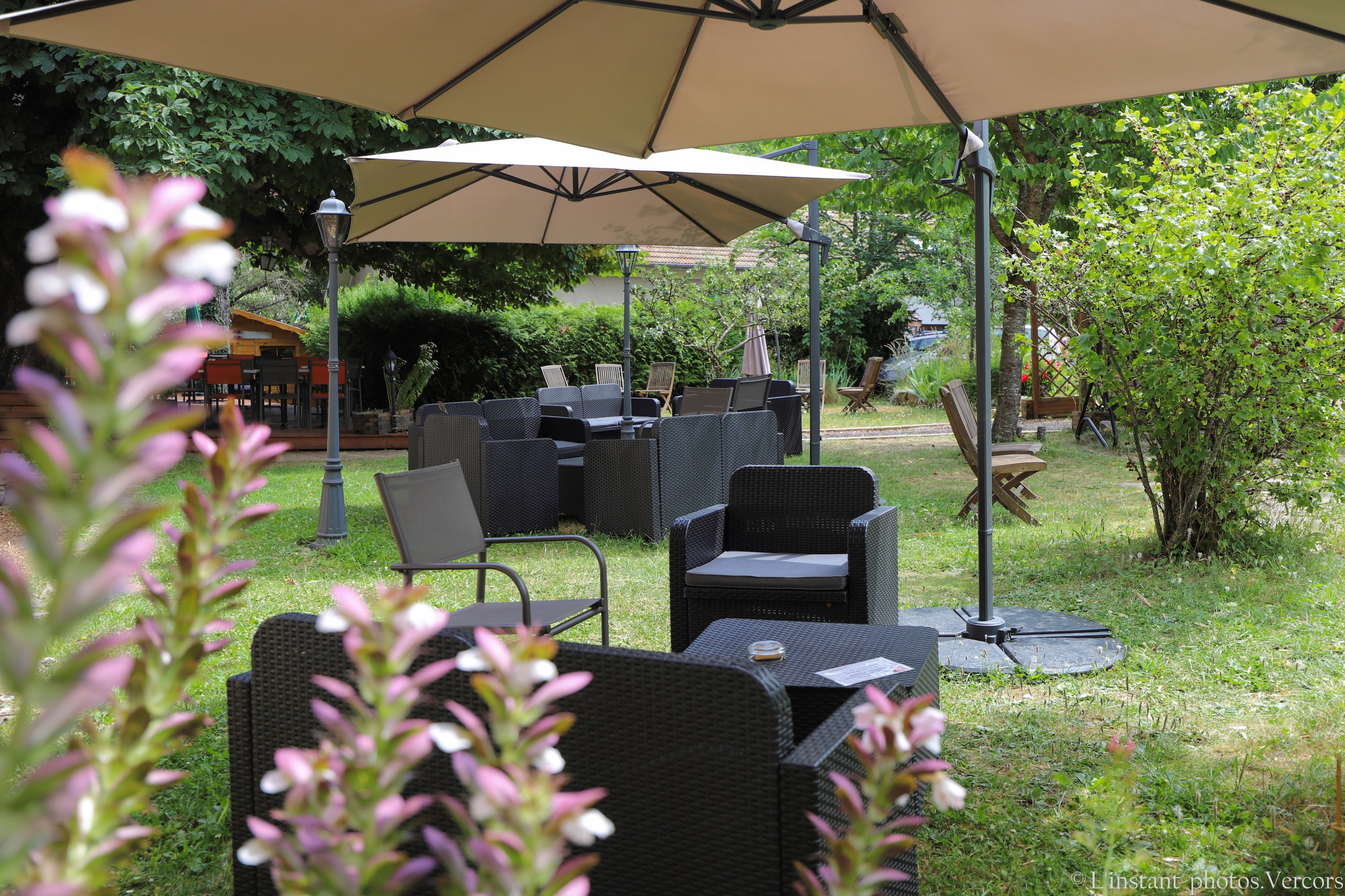 Salons de jardin installés sur la pelouse, abrités par de grands parasols et entourés d’arbres