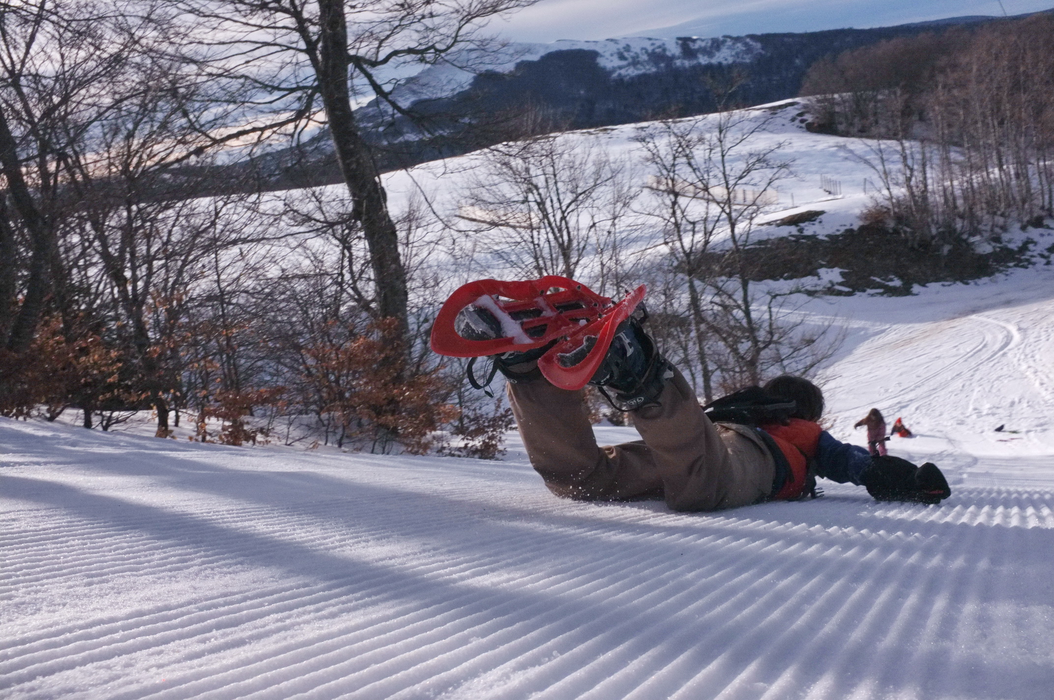 Sur une pente enneigée, une personne fait une glissade sur le ventre, avec ses raquettes à neige aux pieds.