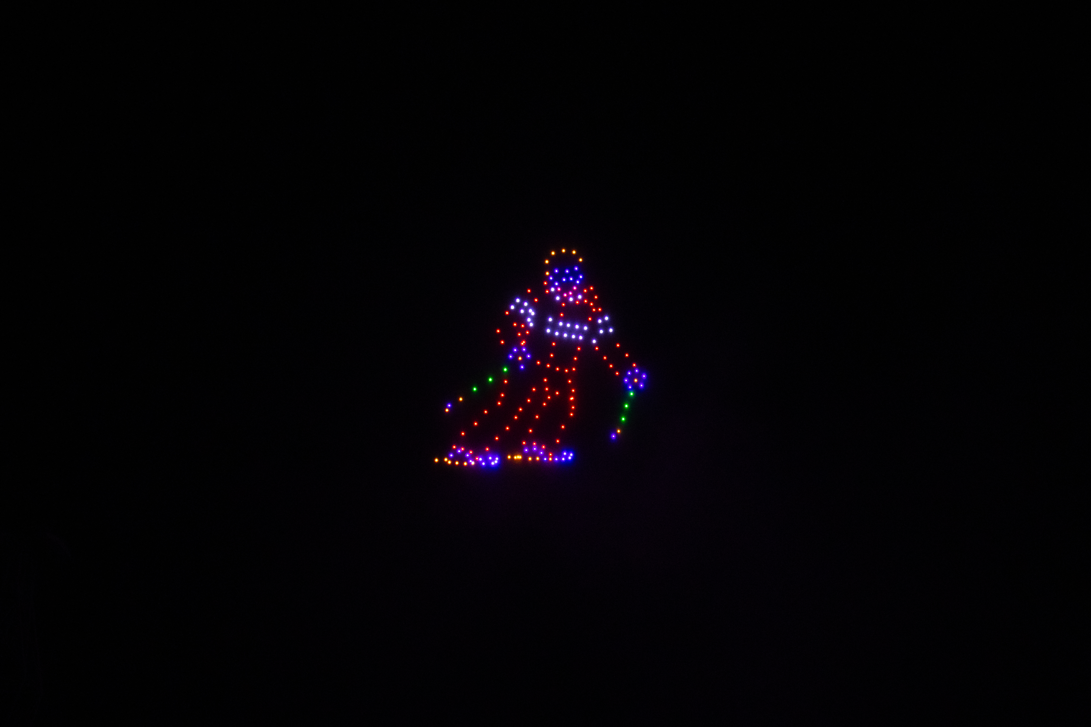 In een volledig zwarte nachtelijke hemel vormen honderden verlichte drones het kleurrijke silhouet van een skiër midden in een bocht.