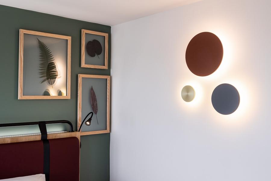 Zoom sur la décoration d'une chambre avec un mur vert et un mur blanc, un miroir et des cadres.