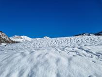 Grande étendue vallonée enneigée, montagnes enneigées en arrière-plan, grand ciel bleu